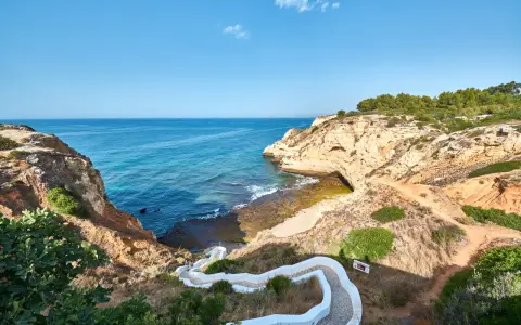 Treppe führt zum malerischen Algarve Meer. Felsformationen und türkisfarbenes Wasser.