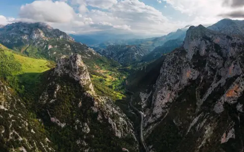 Majestätische Berge der Picos de Europa, grüne Täler und eine Straße, die sich durch die zerklüftete Landschaft schlängelt.