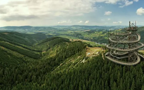 Widok na Sky Walk Czechy, spiralną wieżę widokową pośród zielonych wzgórz i lasów.