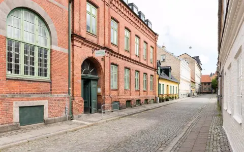 Gammalt tegelhus med gröna fönster och dörrar, en del av ett charmigt vandrarhem i Skåne. Gatsten leder längs en lugn gata.
