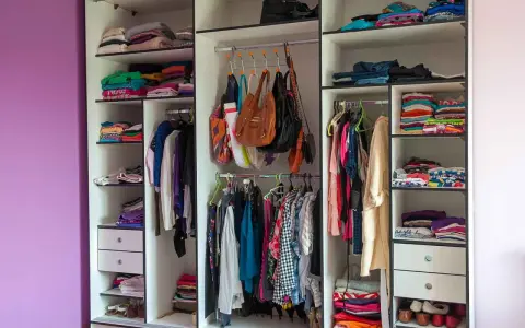 Armadio a muro con ante scorrevoli, pieno di vestiti piegati e appesi, borse e scarpe. Le dimensioni armadio camera da letto sono ben sfruttate.