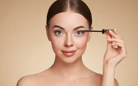 Femme appliquant du mascara sur ses cils, regard bleu intense.