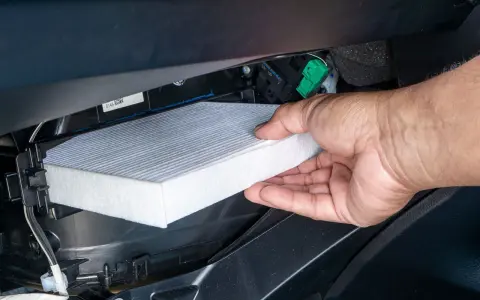 A hand removes a new cabin air filter from its packaging, ready to install it. This shows how to change cabin air filter for cleaner air.
