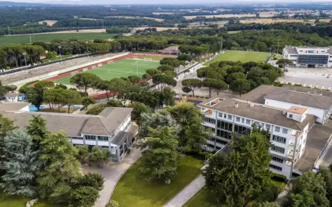 Vista aérea de un colegio Montessori con campos deportivos, piscina y edificios modernos rodeados de árboles.