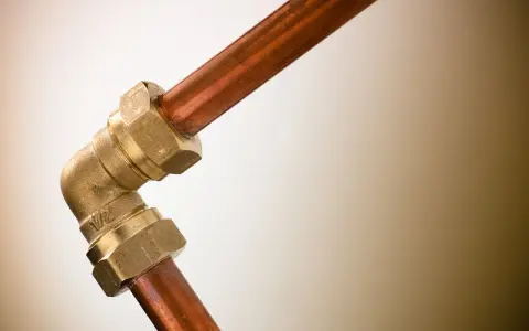 Un coude en laiton relie deux tuyaux en cuivre. Ce raccord per cuivre est essentiel pour les installations de plomberie.