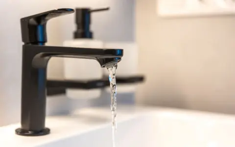 Robinet noir moderne, eau claire coulant dans un lavabo. Un adoucisseur d'eau est peut-être installé pour lutter contre l'eau calcaire.