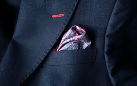 Elegancka poszetka w paisley do granatowego garnituru, z subtelnym czerwonym przeszyciem na klapie.