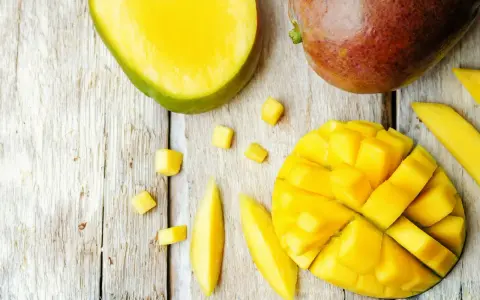 Czy pies może mango? Na drewnianym blacie leżą soczyste kawałki mango, pokrojone w kostkę i paski. Obok całe, dojrzałe owoce.