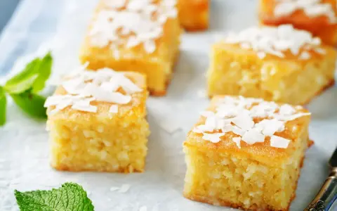 Fette di torta al cocco dorata, guarnite con scaglie di cocco e foglie di menta fresca.