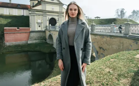 Kobieta w szarym płaszczu i golfie, idealna stylizacja na 14 stopni. W tle zamek i most.