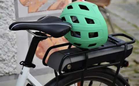Zielony kask na bagażniku roweru elektrycznego, obok siodełka. Baterie do rowerów elektrycznych są gotowe do długiej podróży.