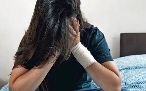 Osoba z opaską na ręce ukrywa twarz we włosach. To przykłady zachowań autodestrukcyjnych, które mogą być wołaniem o pomoc.