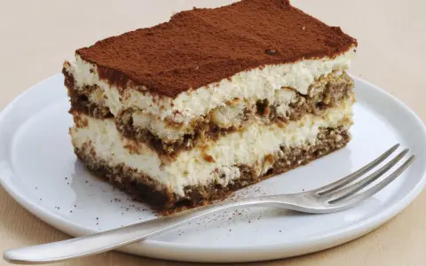 Une part de tiramisu sans oeuf, légère et aérienne, saupoudrée de cacao, sur une assiette blanche avec une fourchette.
