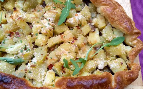 Torta salata patate e cipolle dorata e croccante, guarnita con rucola e peperoncino.