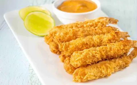 Crujientes gambas a la gabardina doradas, servidas con rodajas de lima y una salsa cremosa.