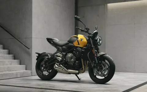 Żółty motocykl Triumph Trident 660 z czarnymi akcentami stoi na betonowej posadzce obok schodów.