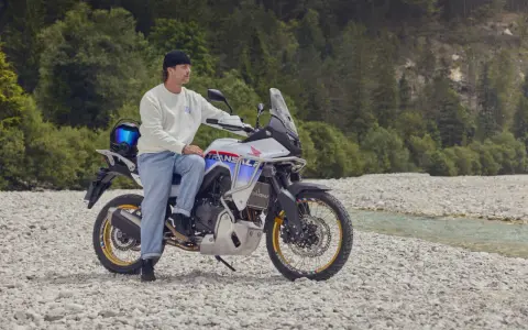Mężczyzna na motocyklu Honda Transalp, gotowy na przygodę motocyklem po Europie. W tle las i strumień.