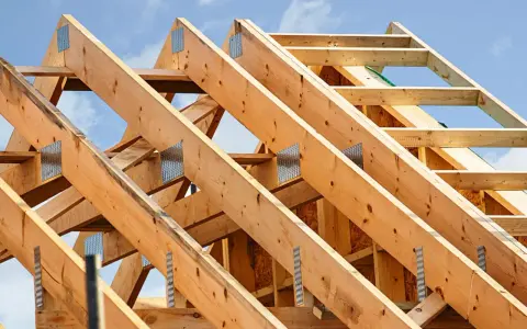 Structure en bois d'une charpente de toiture, avec des poutres assemblées par des connecteurs métalliques sous un ciel bleu.