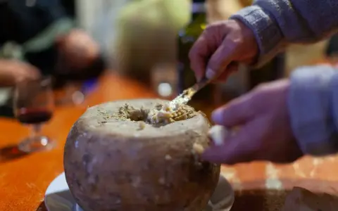 Un uomo serve un formaggio con i vermi, una specialità sarda, con un coltello. Sul tavolo, un bicchiere di vino rosso.