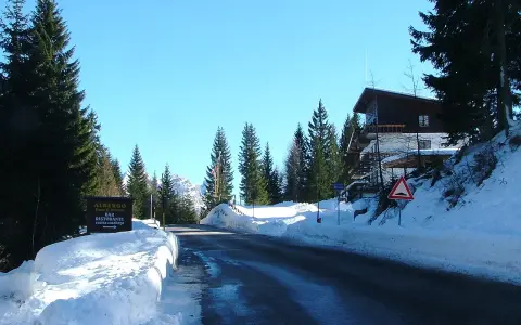 Strada innevata al passo San Antonio. Albergo e ristorante con cucina casalinga. Case di montagna e pini.