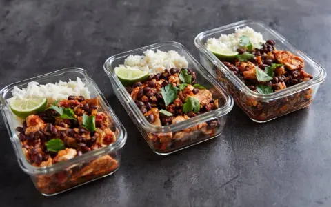 Meal prep für Muskelaufbau: Drei Glasbehälter mit Reis, schwarzen Bohnen, Hähnchen und Limette. Perfekte meal prep muskelaufbau rezepte für deine Fitnessziele.