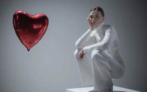 Kobieta w białym stroju siedzi przy czerwonym balonie w kształcie serca, jakby przeżywała zespół Otella.