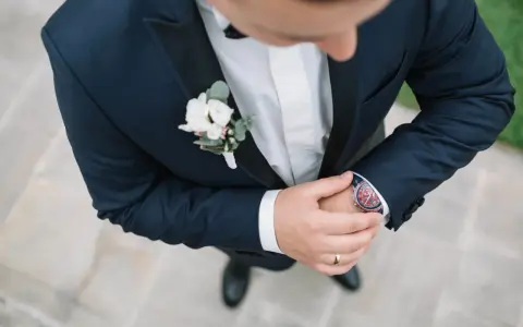 Elegancki pan młody w granatowym garniturze z butonierką co to jest, poprawia zegarek.