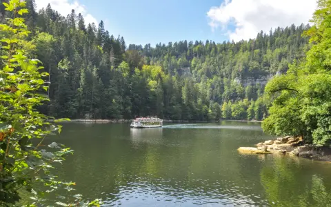 Bateau naviguant sur une rivière bordée de forêts luxuriantes, un paysage typique des chutes du Doubs.