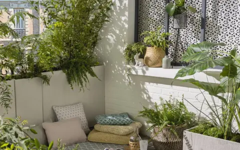 Un coin détente sur un balcon avec une plante brise-vue qui pousse vite en bac, des coussins et des plantes vertes.