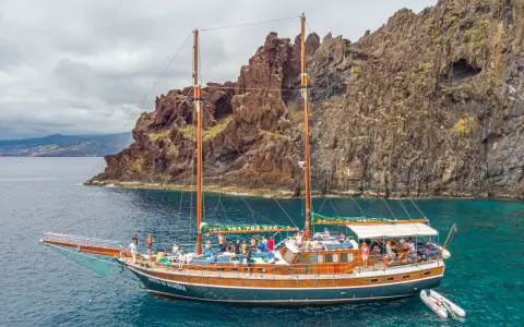 Segelschiff mit vielen Passagieren vor steiler Felsküste, ein Traum für Madeira Segeln.