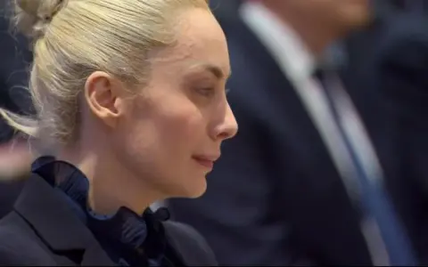 Marta Fascina, con i capelli raccolti, indossa un abito scuro. La sua espressione pensierosa suggerisce un momento di riflessione prima di un evento importante, forse legato a Silvio Berlusconi.