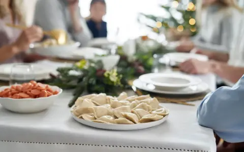 Talerz pierogów i miska z marchewką na wigilijnym stole, w tle rodzina i choinka.