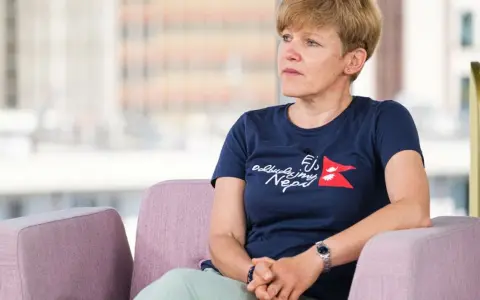 Monika Witkowska w granatowej koszulce z napisem "Odbudujmy Nepal" siedzi w różowym fotelu, patrząc w bok.