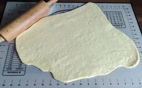Pâte à beignet légère et croustillante étalée sur un tapis de pâtisserie avec un rouleau à pâtisserie en bois.