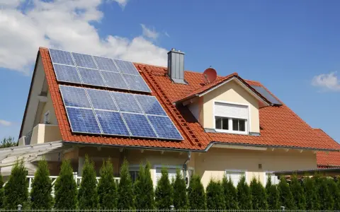 Dom z czerwoną dachówką i panelami fotowoltaicznymi. Mikroinstalacja PV na dachu zapewnia czystą energię.
