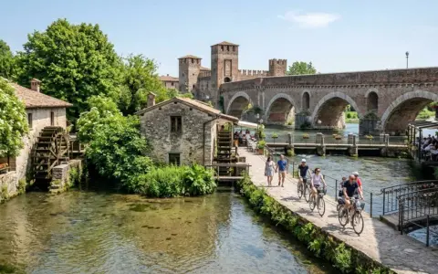 Un pittoresco borghetto sul Mincio con mulini ad acqua, un ponte ad archi e persone che passeggiano e pedalano.