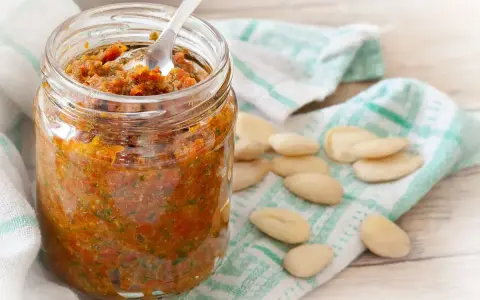 Vasetto di pesto di pomodori secchi, con mandorle sparse su un canovaccio.