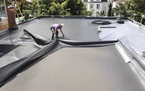 Pose d'une membrane d'étanchéité pour l'isolant toit plat. Un ouvrier déroule la bâche noire sur le toit.