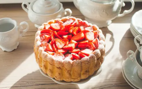 Gâteau frais garni de fraises, entouré de biscuits cuillère et saupoudré de sucre glace. Une belle table de thé.