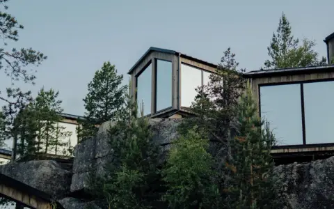 Moderna trähus med stora fönster klättrar uppför en stenig sluttning, omgivna av tallar. En idyllisk camping Lapland resort.