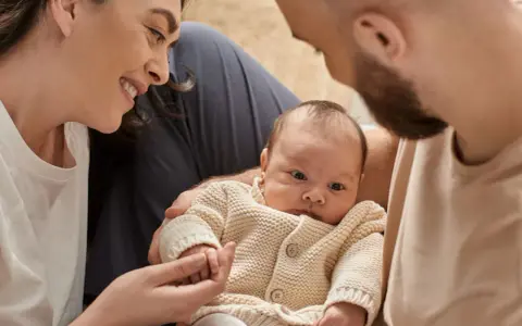 Una madre sonríe a su bebé, mientras el padre lo abraza. A pesar de que mi bebé no tiene apego conmigo, la familia se ve unida.