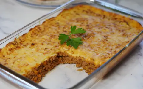 Pastel de papa recién horneado en refractario de vidrio, con una porción retirada, decorado con perejil fresco.