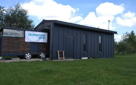Mobilny garaż bez pozwolenia, z napisem "Zbuduj sam dom", stoi na trawie.