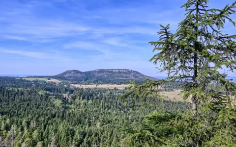 Widok na górzysty krajobraz z lasami i polami, w oddali widać płaskie wzgórze przypominające fort Karola.