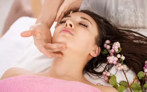 A woman receives an anti aging facial massage, her eyes closed in relaxation. Delicate pink berries adorn her dark hair.