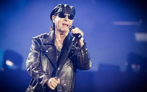 Klaus Meine, jung und rockig, singt ins Mikrofon, trägt Lederjacke und Kappe.