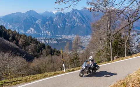 Motociclista in un panoramico motogiro Lombardia, con montagne maestose e un lago sullo sfondo.