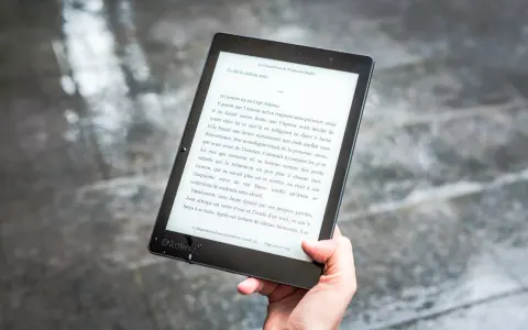 Ręka trzyma czytnik ebooków z tekstem. Czytanie książek elektronicznych to przyjemność, a teraz dzięki zmianom w prawie, vat na ebooki jest korzystniejszy.