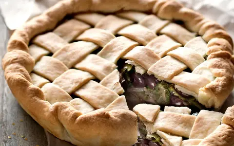 Pizza di scarola con un intreccio dorato di pasta, ripiena di verdure e olive. Un sapore autentico.