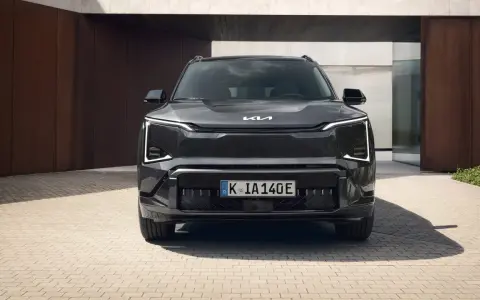Szary SUV Kia EV5 z charakterystycznymi światłami LED, zaparkowany przed nowoczesnym budynkiem.